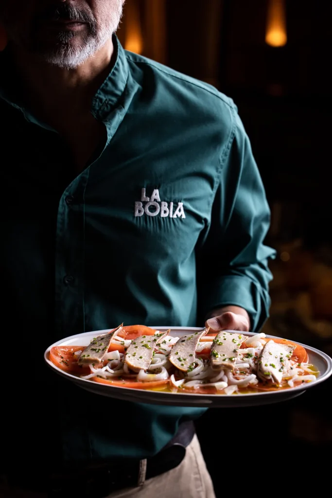 Camarero de La Bobia sirviendo ensalada de tomate de la huerta con cebolleta tierna y ventresca de atún, plato de cocina asturiana tradicional en Madrid